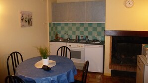 Une cuisine compacte équipée d’une cuisinière, d’un évier et d’un crédence à carreaux. On y trouve une table à manger avec des chaises et une petite plante en pot.