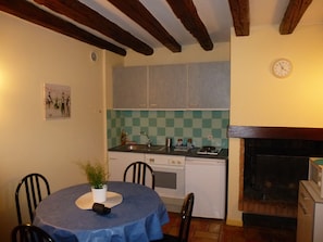 Une cuisine compacte équipée d’une cuisinière, d’un évier et d’un crédence à carreaux. On y trouve une table à manger avec des chaises et une petite plante en pot.