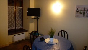 Un coin repas avec une table recouverte d’une nappe bleue, une plante en pot et un téléviseur à écran plat fixé au mur.