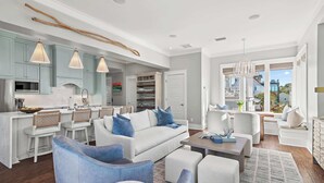 A modern living room with a white sofa, blue armchairs, and a coffee table. There is a kitchen area with light blue cabinets and a dining table with bar stools. - New Reno!- Steps to Beach- Elevator- Golf Cart (Santa Rosa Beach)