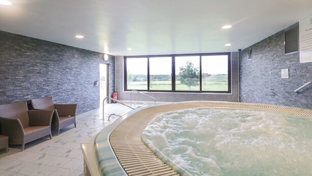 Ett spaområde med ett bubbelbad, sittplatser och ett stort fönster med utsikt över omgivningen.
