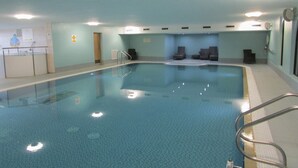 En inomhuspool med klart vatten, en hoppställning och flera solstolar.