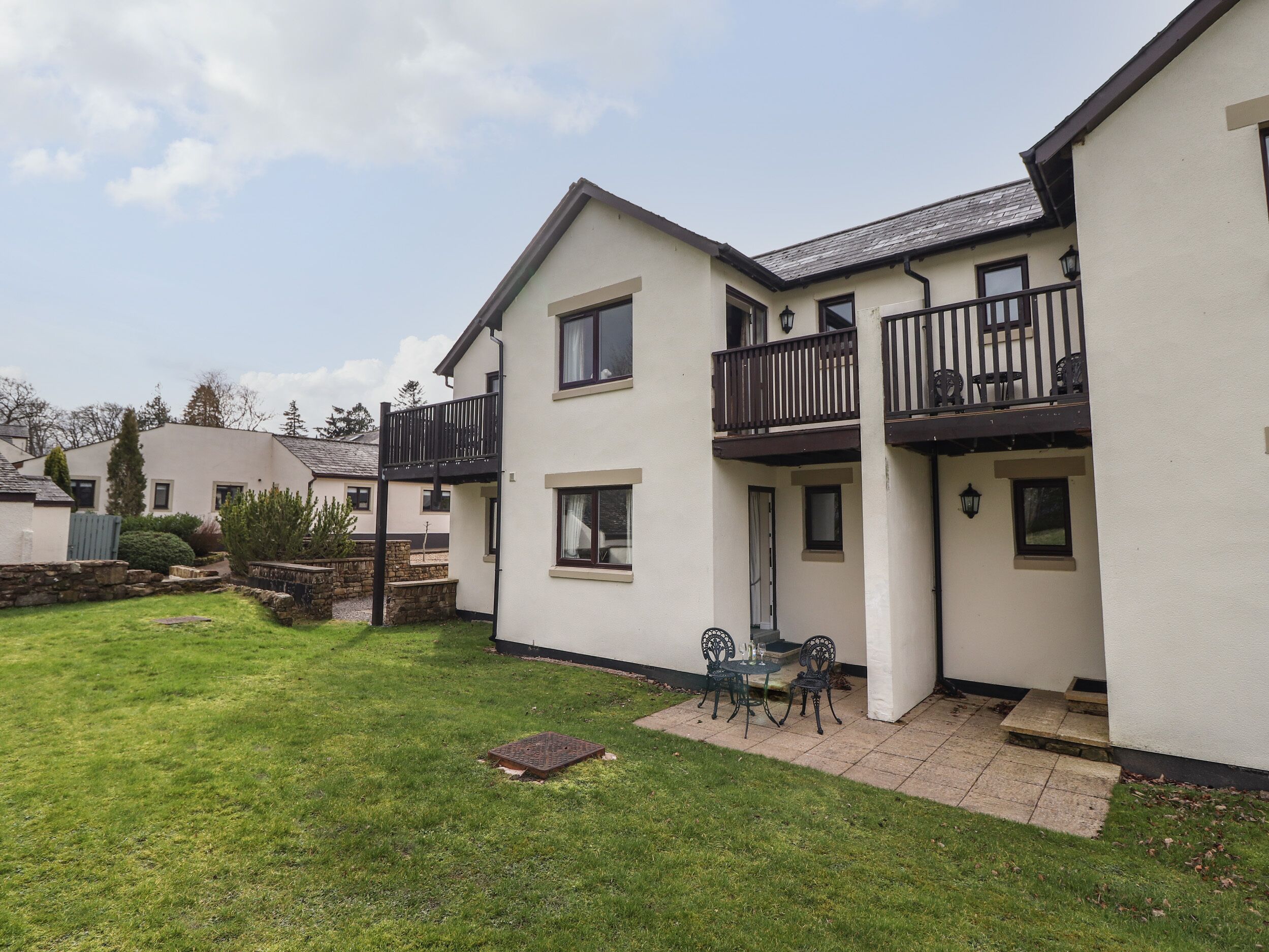 A two-story residential building with a balcony, a small patio with outdoor furniture, and a well-maintained lawn.