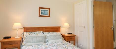 A bedroom with a bed, two bedside tables, a nightstand, a wooden door, and a framed picture on the wall.