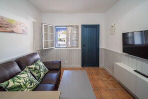 A compact living space with a sofa, a television, a door, and a window. - Green Coast (Punta Mujeres)
