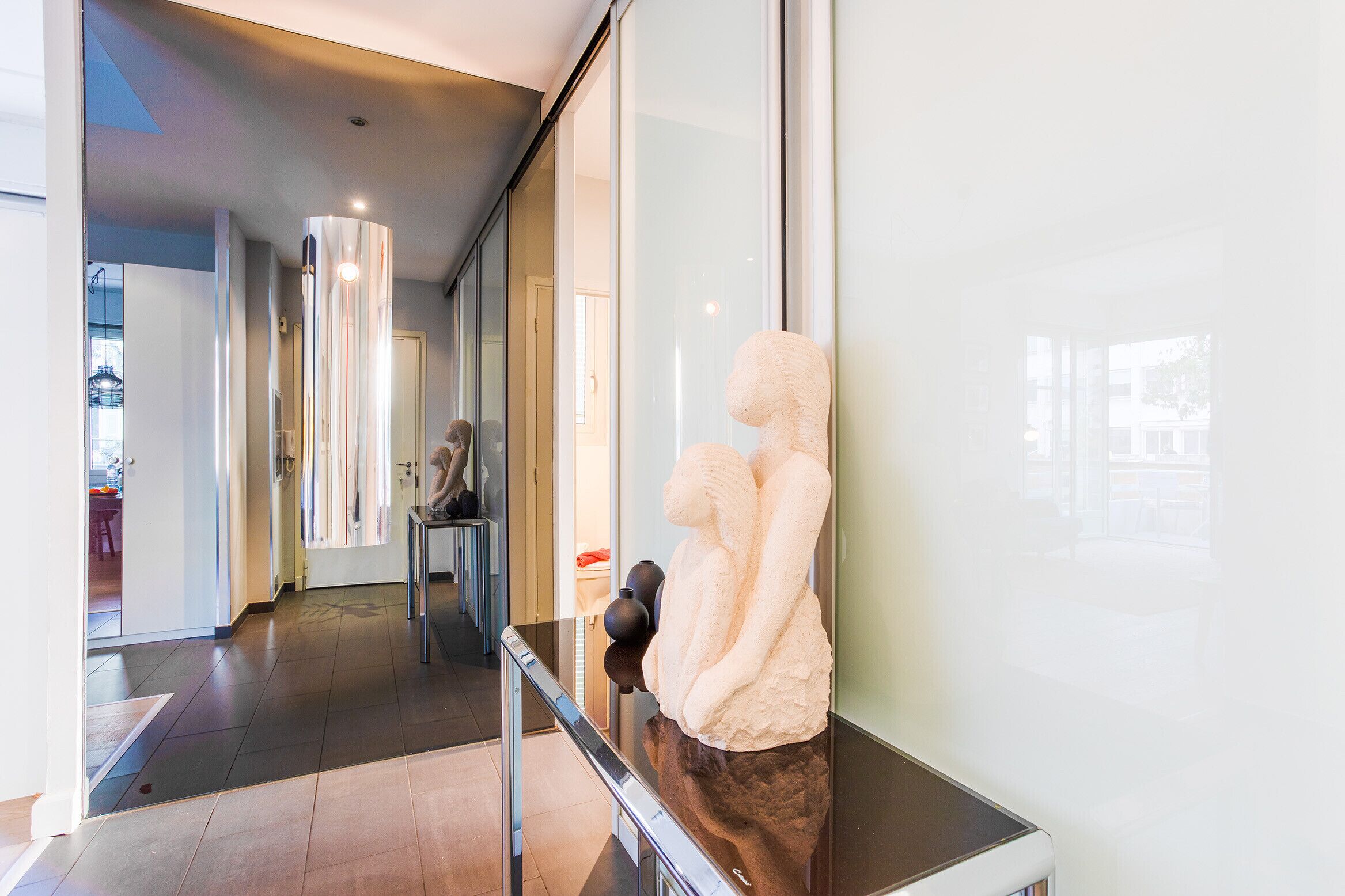 A modern hotel corridor with a glass wall, a sculpture, and a bench.