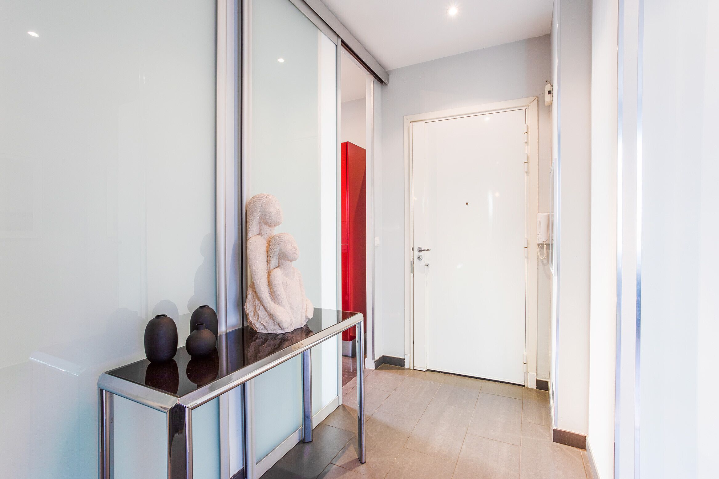 A modern hallway with a glass partition, a white door, and a red accent wall.