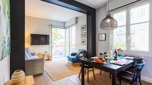 Ein modernes Wohnzimmer mit Essbereich, großen Fenstern und einem Flachbildfernseher.