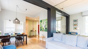 Ein modernes Wohnzimmer mit einem weißen Sofa, einem Essbereich mit Tisch und Stühlen sowie einer Küche im Hintergrund.