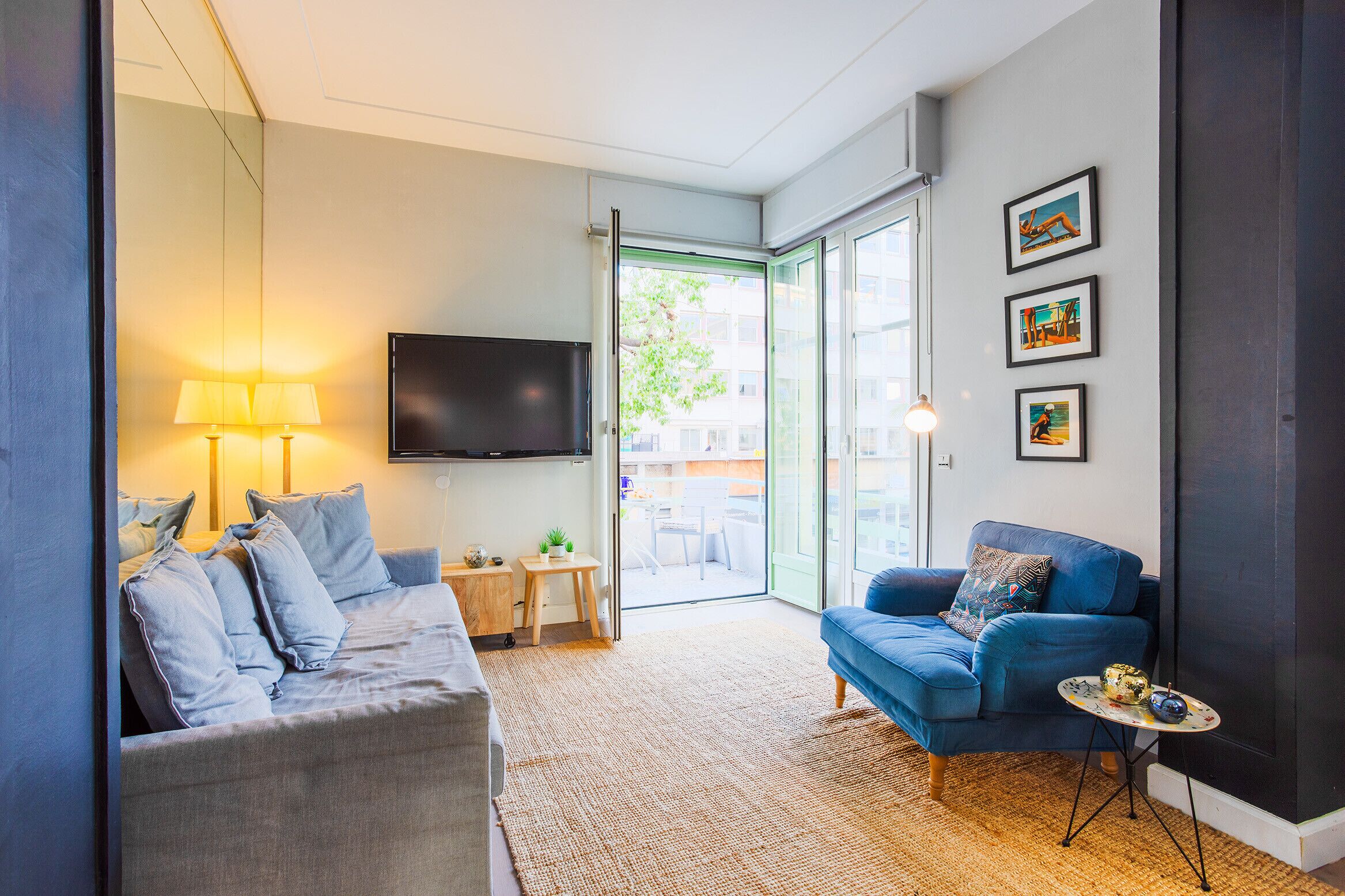 A modern living room with a grey sofa, a blue sofa, a small round table, and a TV mounted on the wall.