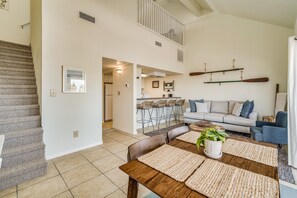 A spacious living area with a staircase, a dining table with placemats, a sofa, and a kitchen in the background.