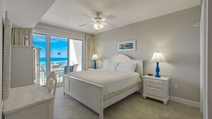 A bedroom with a bed, two bedside tables with lamps, a ceiling fan, a view of the ocean, and a balcony with a chair. - Ariel Dunes II 1808  *Gulf views*Pools*Beach access (Destin)