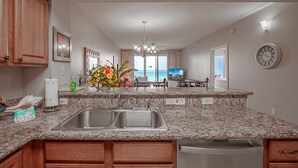 A kitchen with granite countertops, a double sink, wooden cabinets, and a view to the living area. - Ariel Dunes II 1808  *Gulf views*Pools*Beach access (Destin)