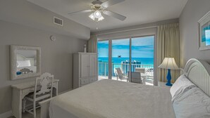 A hotel room with a large bed, a desk with a chair, a ceiling fan, a large window with a view of the ocean, and a balcony with a chair and table. - Ariel Dunes II 1808  *Gulf views*Pools*Beach access (Destin)