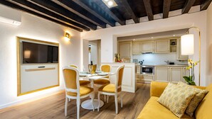 Une cuisine moderne avec des meubles blancs et un îlot central, un coin repas avec des chaises jaunes et une table blanche, et un canapé jaune agrémenté de coussins à motifs.