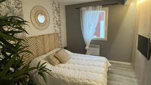 Ein Schlafzimmer mit Bett, Nachttisch, einem Fenster mit durchsichtigen Vorhängen und einer Wand-Klimaanlage.