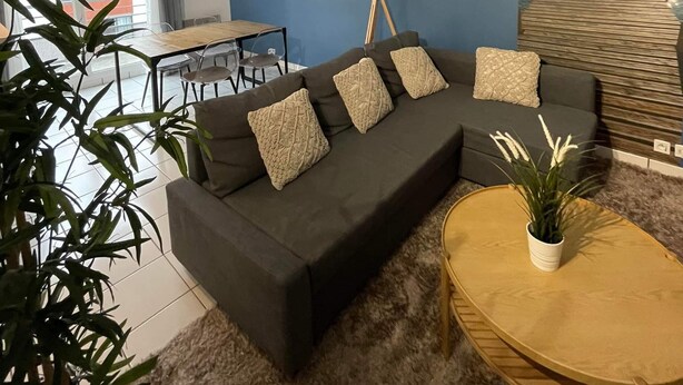 Ein modernes Wohnzimmer mit einem dunkelgrauen Sofa, einem runden Couchtisch und einem großen Fenster.