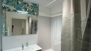 Ein modernes Badezimmer mit einem weißen Waschbecken, Holzschränken, einem großen Spiegel und einer Dusche mit Duschvorhang.