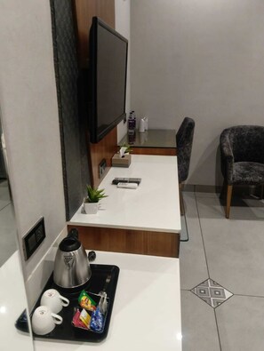 A modern hotel room with a flat-screen TV, a small desk with a plant, a chair, and a coffee station.