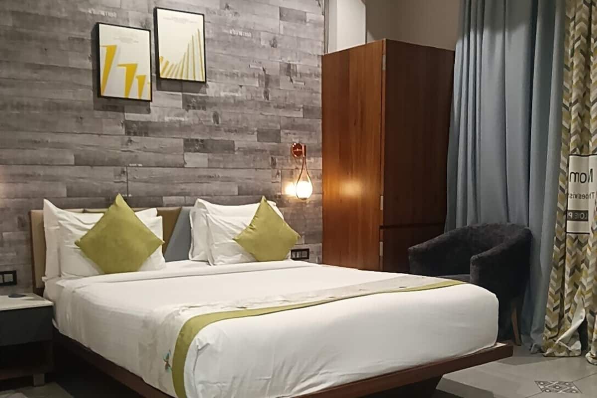 A modern hotel room with a large bed, a wardrobe, a nightstand, and a wall-mounted light fixture.
