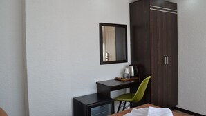 A hotel room with a bed, a desk with a chair, a small refrigerator, a mirror, and a wardrobe. - Global 2022 Hotel (Istanbul)