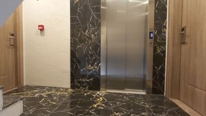 A modern elevator with a marble finish, a wooden door, and a red emergency button. - Global 2022 Hotel (Istanbul)
