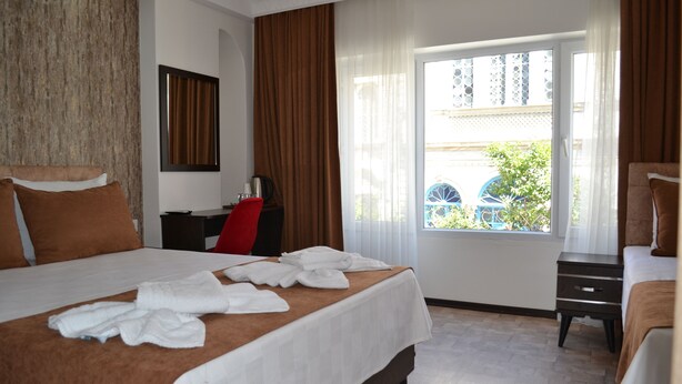 A hotel room with a large bed, a desk, a chair, and a window with a view of greenery. - Global 2022 Hotel (Istanbul)