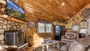 Een gezellig interieur van een chalet met een stenen openhaard, leren bank en een televisie aan de muur.