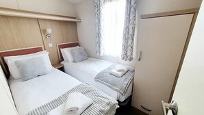 Et hotelværelse med to senge, et træsengegærde, et vindue med gardiner og en dør.