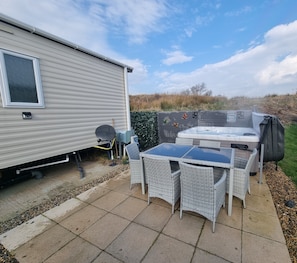 Ein Wohnwagen mit einer Terrasse, komplett mit Tisch, Stühlen, einem Whirlpool und einem Grill.