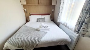 Ein ordentlich gemachtes Bett mit weißen Leinentüchern, einem Kissen mit Schriftzug und einem gefalteten Handtuch.