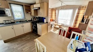 Et lille køkken med mikrobølgeovn, brødrister og komfur. Der er et spiseområde med bord og stole, samt en rød sofa.