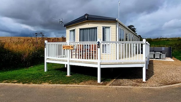 En mobilbolig med hegnede terrasse, parabolantenne og grusvej.