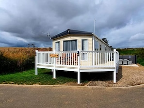 Ein Mobilheim mit umzäunter Terrasse, Satellitenschüssel und Kiesweg.