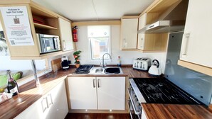 A compact kitchen with a microwave, toaster, kettle, and stove. There is a sink, a potted plant, and a fire extinguisher. A sign with WiFi instructions is visible on the wall. - Apple Tree Lodge, Hot Tub, 3 Bedroom, 2 Bars (Morpeth)
