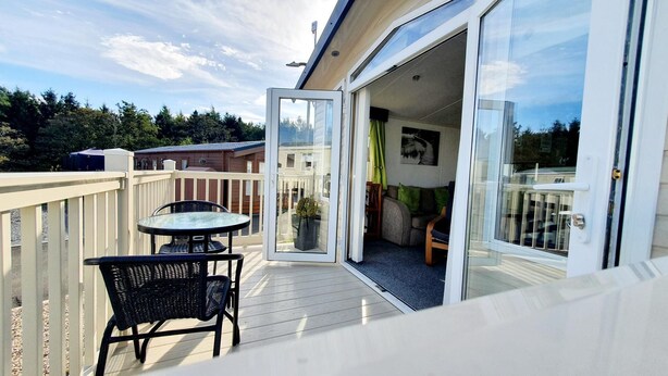 A balcony with a table and chairs, a sliding glass door leading to an interior space with a couch and a plant. - Apple Tree Lodge, Hot Tub, 3 Bedroom, 2 Bars (Morpeth)