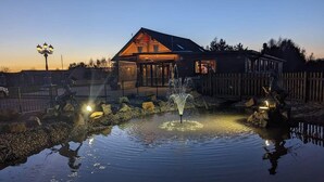 A wooden cabin with a pond and fountain, surrounded by a fence and trees. - Apple Tree Lodge, Hot Tub, 3 Bedroom, 2 Bars (Morpeth)