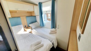 A compact bedroom with two beds, a wooden headboard, a small bedside table, and a window with curtains. - Apple Tree Lodge, Hot Tub, 3 Bedroom, 2 Bars (Morpeth)