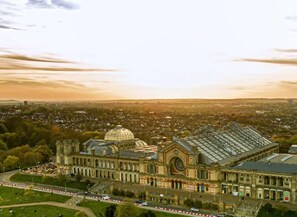 A large, historic building with a prominent dome and arched windows, surrounded by a cityscape and greenery.