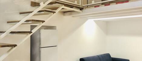 A modern interior with a dining area, a sofa, and a staircase leading to an upper level.