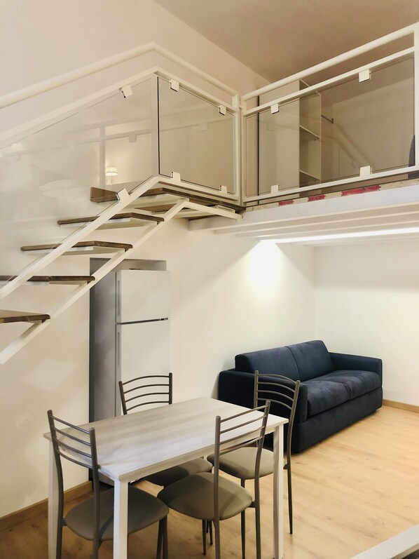A modern interior with a dining area, a sofa, and a staircase leading to an upper level.