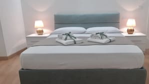 A double bed with a grey headboard, two bedside tables with lamps, and neatly folded towels on the bed. - B&B in the wonderful and evocative center of Rodi Garganico (Rodi Garganico)