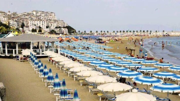 A beach with rows of sun umbrellas and lounge chairs, a building in the background, and a view of the sea. - B&B in the wonderful and evocative center of Rodi Garganico (Rodi Garganico)