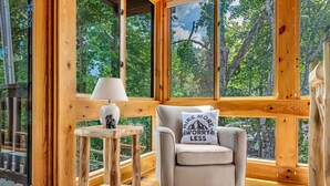 A wooden cabin interior with a sofa, a lamp, and a view of the forest. - Riverfront, ½ Mile to Smoky Mtn National Park (Townsend)