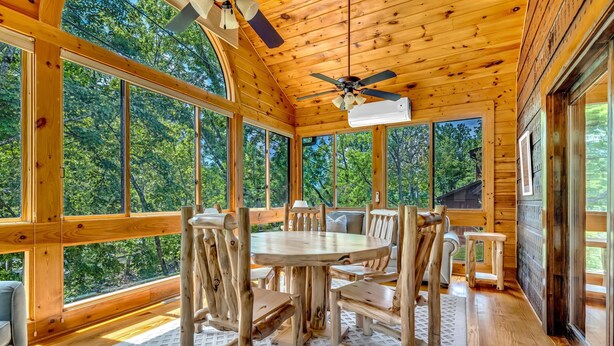 A wooden cabin with a dining area featuring a round table and chairs, large windows, and a ceiling fan. - Riverfront, ½ Mile to Smoky Mtn National Park (Townsend)