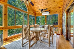 A wooden cabin with a dining area featuring a round table and chairs, large windows, and a ceiling fan. - Riverfront, ½ Mile to Smoky Mtn National Park (Townsend)