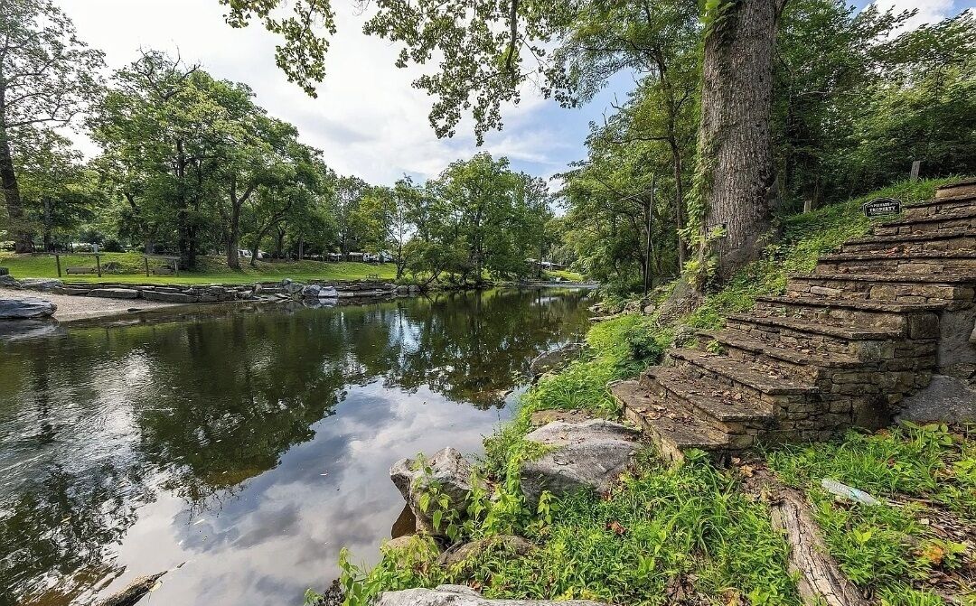 Un parc tranquil amb un estany, escales de pedra i vegetació exuberant.