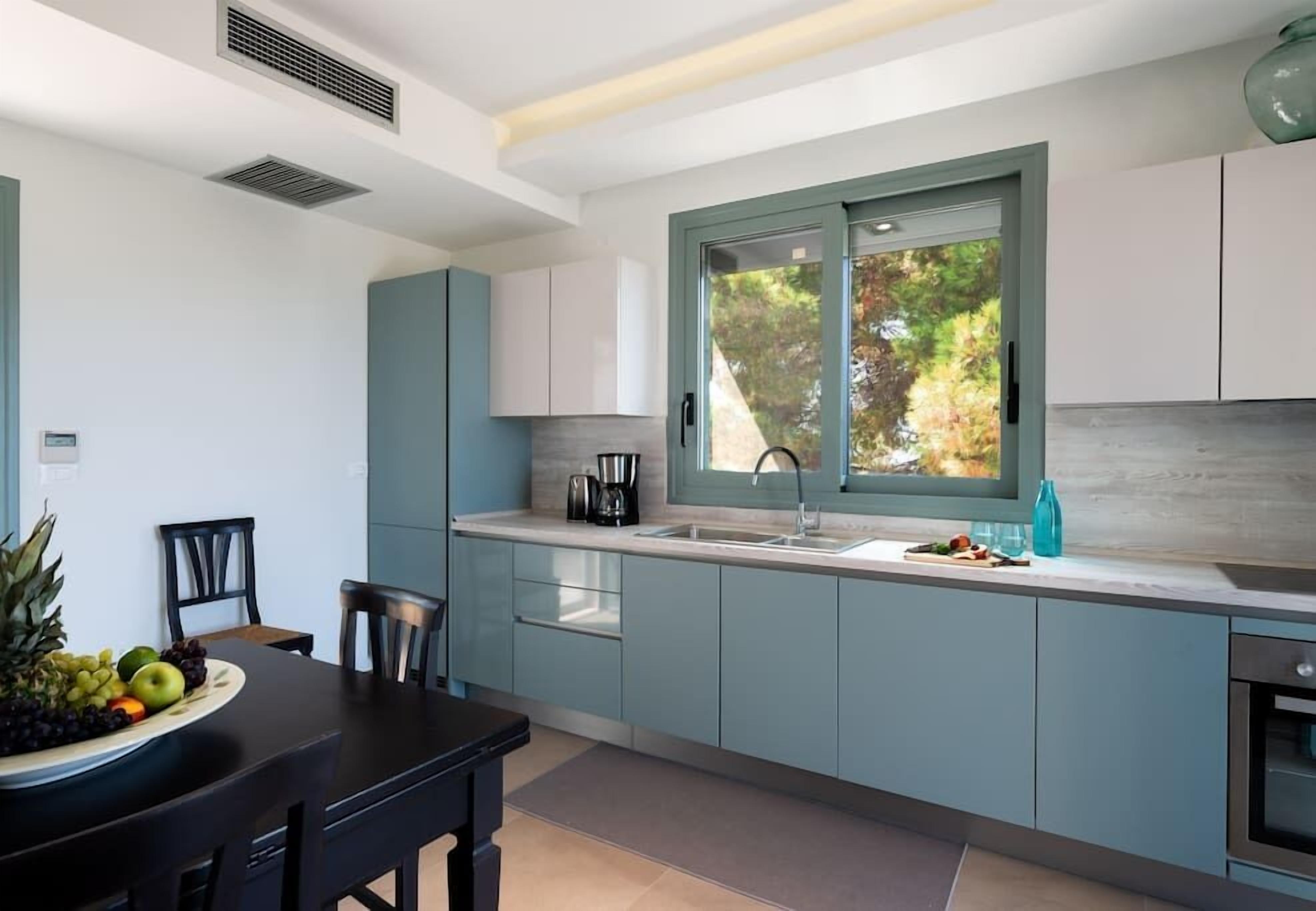 Une cuisine moderne avec des meubles de couleur bleu clair, un plan de travail noir et une fenêtre donnant sur des arbres.