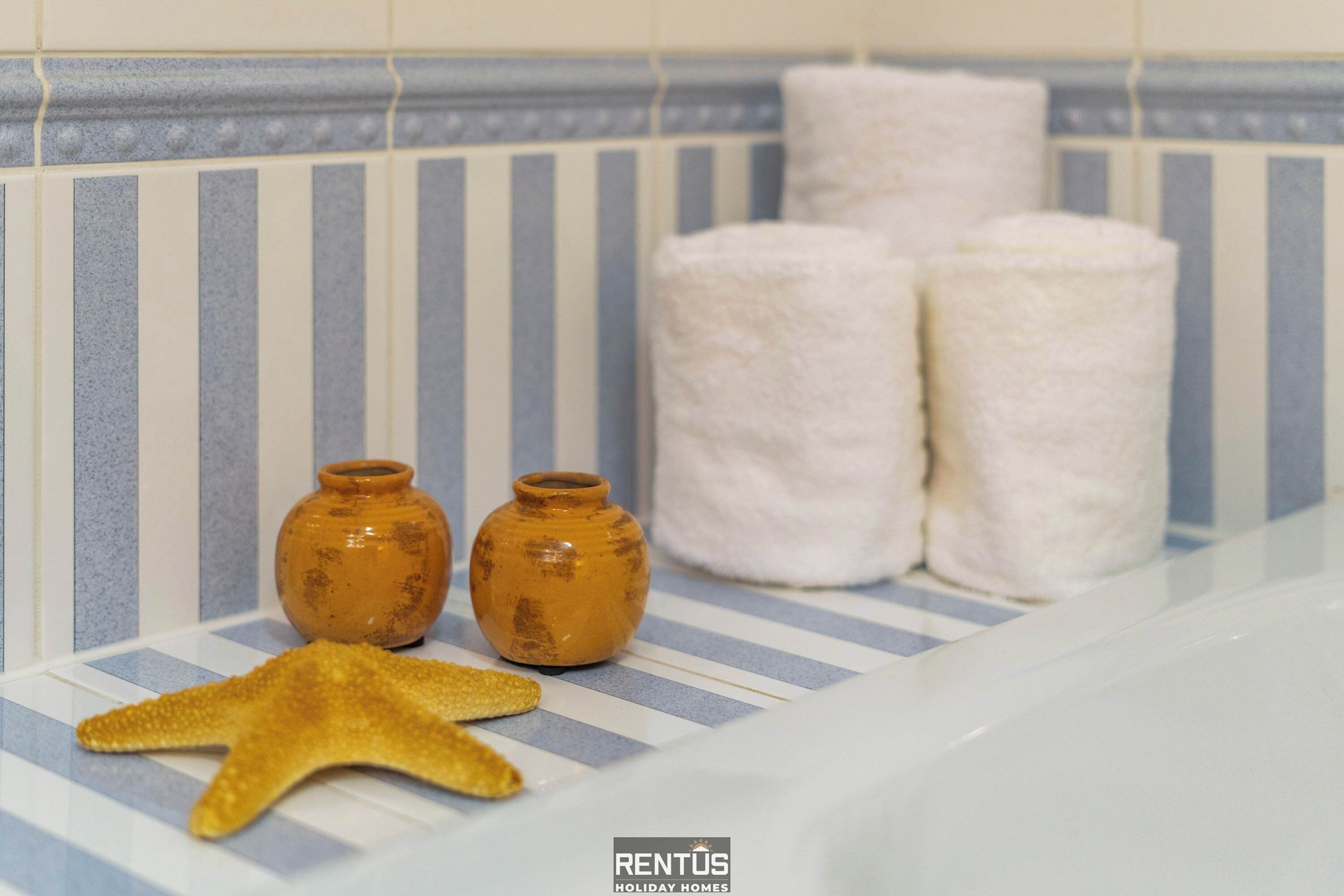 Een badkamer met streepmotief tegels, twee kleine terracotta potten, een zeester en twee toiletrollen.