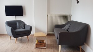 A modern living room with two grey sofas, a flat-screen TV, a radiator, and a small wooden table with a basket. - House (Dornum)
